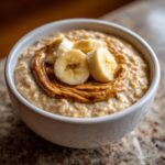 Close-up of creamy banana oatmeal topped with a swirl of peanut butter and fresh banana slices.