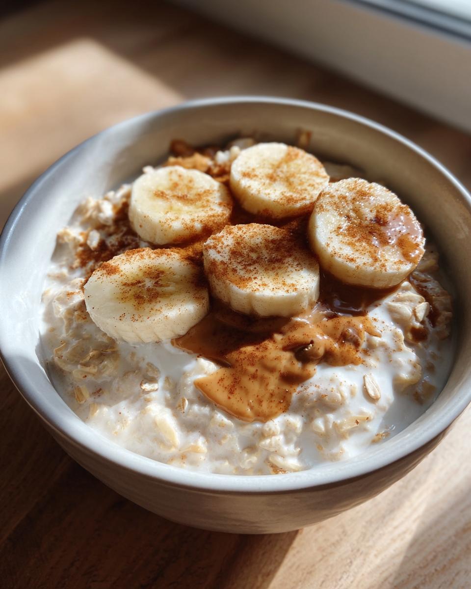 Close-up of creamy banana oatmeal topped with sliced bananas, peanut butter drizzle, and cinnamon.