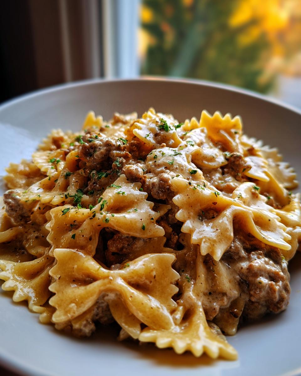 A close-up shot of creamy beef pasta made with farfalle (bowtie) noodles, topped with parsley.