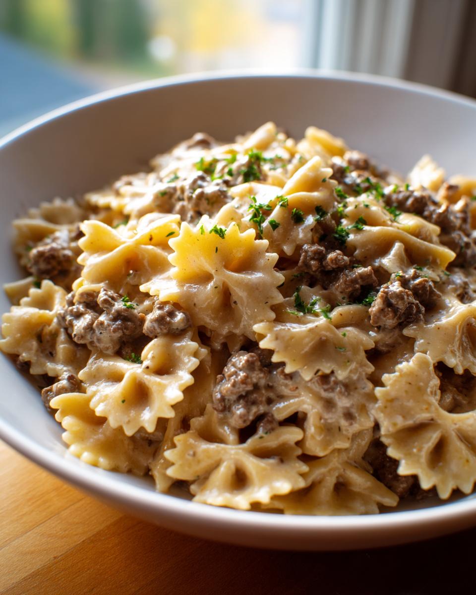 Close-up of a white bowl filled with creamy beef pasta made with farfalle (bowtie) noodles and ground beef.