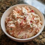 Close-up of a creamy, chunky boat dip mixed with red peppers and green herbs served in a white bowl.