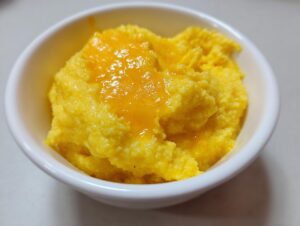 Close-up of a small white bowl filled with creamy, bright yellow cheese grits topped with melted cheddar.