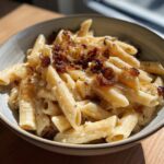 Close-up of creamy penne pasta topped generously with dark, rich caramelized onion pasta.