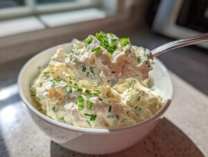 A spoonful of creamy clam dip topped with fresh chives being lifted from a white bowl.