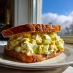 A thick sandwich overflowing with creamy egg salad recipe filling and celery chunks on toasted bread.