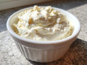 A close-up of thick, creamy homemade garlic sauce speckled with herbs in a small white ramekin.