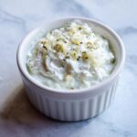 A close-up of creamy homemade garlic sauce topped with minced garlic and herbs in a white ramekin.