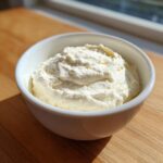 A white bowl filled with freshly made, fluffy creamy horseradish sauce, sitting on a wooden surface.