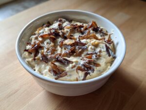 A white bowl filled with creamy onion dip, generously topped with dark, caramelized onions.