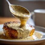 A spoonful of creamy peppercorn sauce is being drizzled over a seared piece of meat.