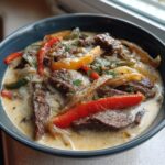 A close-up of a rich, creamy philly cheese steak soup filled with sliced steak, peppers, and onions.