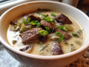 Close-up of a creamy bowl of philly cheese steak soup topped with chunks of steak and fresh green onions.