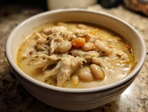 Close-up of a bowl of creamy white chicken chili featuring shredded white chicken, cannellini beans, and carrots.
