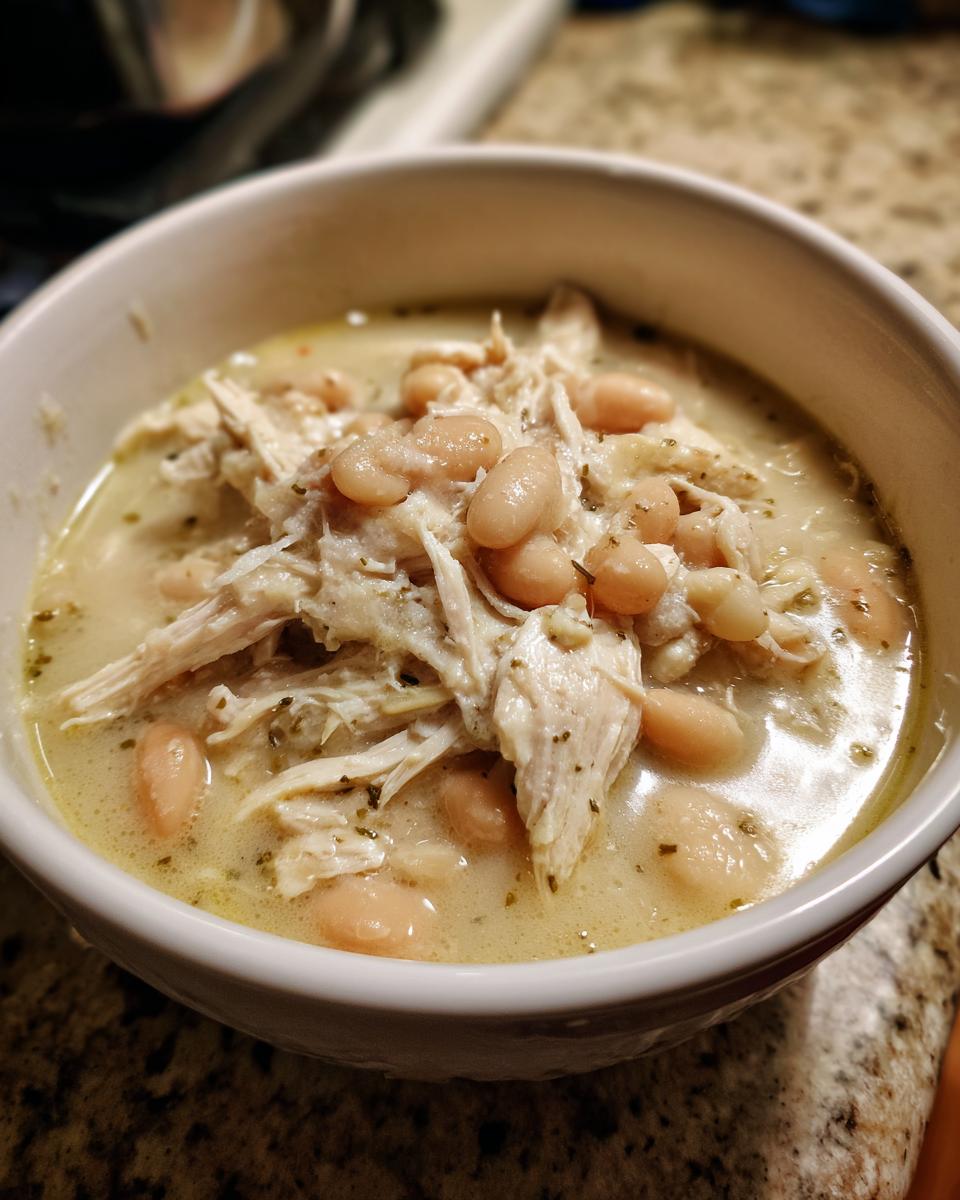 Close-up of a bowl of creamy white chicken chili, featuring shredded white chicken and cannellini beans.