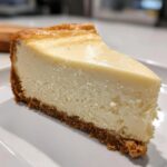 A perfect slice of super creamy white chocolate cheesecake with a thick graham cracker crust on a white plate.