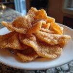 Close-up of a pile of freshly fried, crispy buñuelos coated heavily in cinnamon sugar.