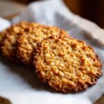 Two golden brown, crispy oatmeal lace cookies resting on parchment paper.