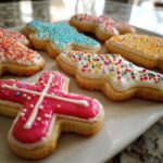 Close-up of several cross-shaped sugar cookies decorated with bright, hardened cookie icing and sprinkles.