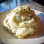 A mound of creamy, fluffy Boursin mashed potatoes garnished with chopped green herbs.