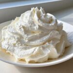 A close-up of perfectly piped, fluffy cream cheese frosting piled high in a white bowl.