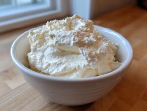 A white bowl filled with fluffy, white creamy horseradish sauce resting on a wooden countertop.