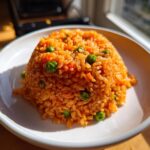 A perfectly molded serving of fluffy mexican rice, bright orange from tomato, mixed with green peas, served in a white bowl.