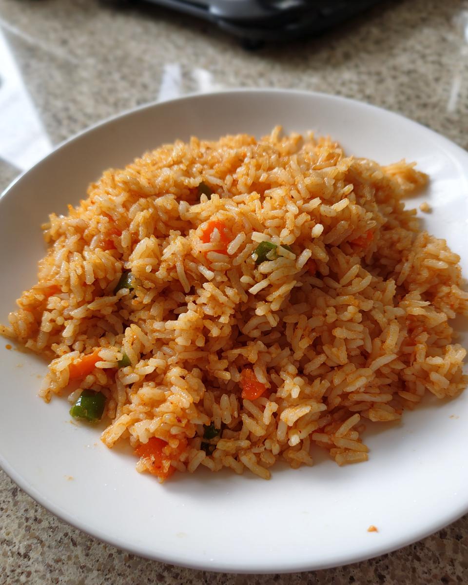 A close-up of fluffy, reddish-orange Mexican rice mixed with visible pieces of diced carrots and green peppers on a white plate.