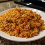 A close-up of a generous serving of vibrant orange Mexican rice with visible pieces of tomato and green peppers.