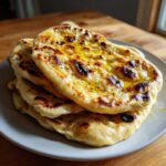A stack of freshly cooked, soft naan bread recipe rounds brushed generously with melted butter.