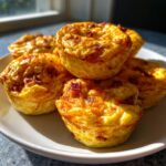 A stack of five fluffy, golden-brown protein egg bites with visible bacon pieces, served on a white plate.
