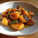 A bowl of perfectly pan-seared sweet potato gnocchi topped with crispy sage leaves and brown butter sauce.
