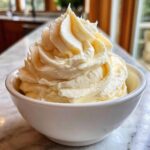 A close-up of perfectly piped, fluffy vanilla buttercream frosting mounded high in a small white bowl.