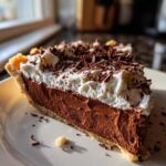 A decadent slice of french silk pie featuring a thick chocolate filling, topped with whipped cream and chocolate shavings.