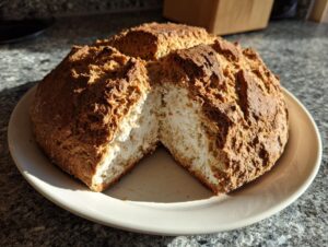 A rustic loaf of freshly baked soda bread, split open to show the soft interior, sitting on a white plate.