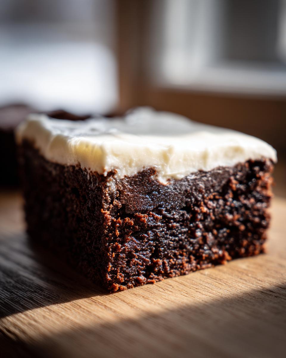 A close-up, side view of a rich, dark gingerbread brownies square topped with thick white cream cheese frosting.