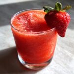 Close-up of a vibrant, frozen strawberry daiquiri garnished with a fresh whole strawberry.