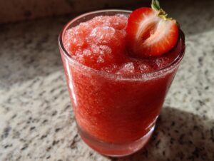 Close-up of a vibrant, frozen strawberry daiquiri garnished with a fresh strawberry slice.