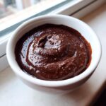 Close-up of thick, rich, dark brown chocolate dip with a slightly textured surface in a small white bowl.
