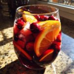 Close-up of a glass filled with vibrant christmas sangria, loaded with orange slices and whole cranberries.