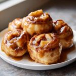 A stack of warm, gooey apple dumpling rolls covered in a rich caramel glaze, served on a white plate.