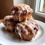 A stack of three golden brown baked apple fritters generously drizzled with white vanilla glaze.