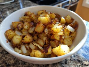 A close-up of golden brown fried potatoes mixed with sautéed onions served in a white bowl.