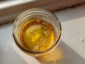 Overhead close-up of golden, viscous liquid, likely oil or honey, in a small glass jar, an ingredient for homemade salad dressing.