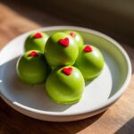 A pile of bright green Grinch Oreo balls, each topped with a small red heart candy, sitting on a light plate.