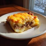 A hearty slice of hamburger potato casserole featuring layers of potatoes, ground beef, and a golden melted cheese topping.