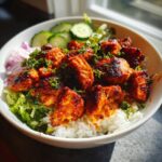 Close-up of a bowl featuring vibrant, spicy harissa chicken pieces served over white rice and lettuce.
