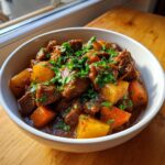 Close-up of a hearty bowl of rich pork stew with chunks of meat, potatoes, and carrots, topped with fresh parsley.