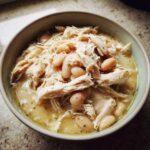 A close-up overhead shot of a hearty bowl of white chicken chili, featuring shredded white chicken and white beans in a creamy broth.