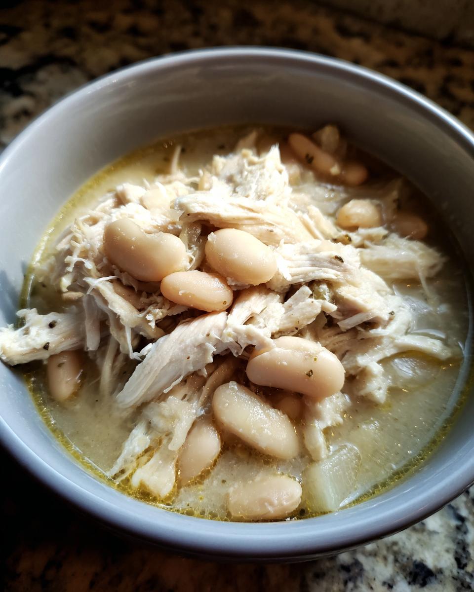 A close-up of a bowl of creamy white chicken chili, featuring shredded white chicken and cannellini beans.
