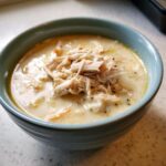A close-up of a bowl of rich, creamy cream of chicken soup generously topped with shredded chicken.